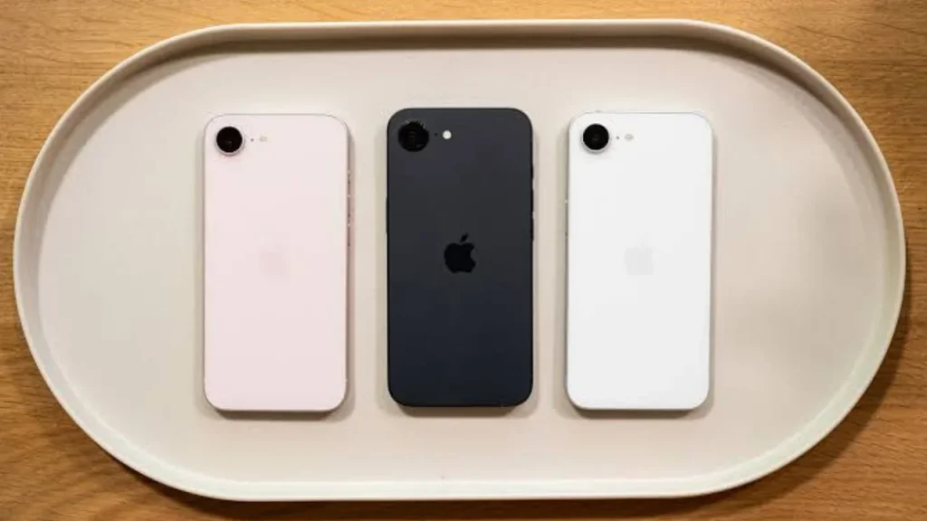 Three Apple iPhone 17e smartphones in light pink, black, and white lying side-by-side on an oval white tray.