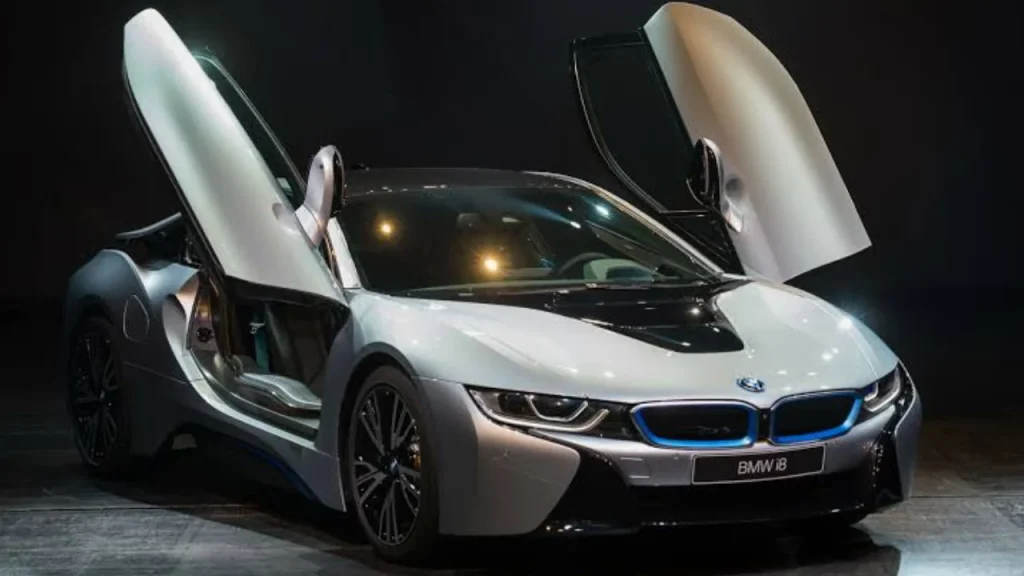 A silver BMW electric sports car with its distinctive scissor doors open in a showroom setting, illustrating luxury from the Best EV brands.
