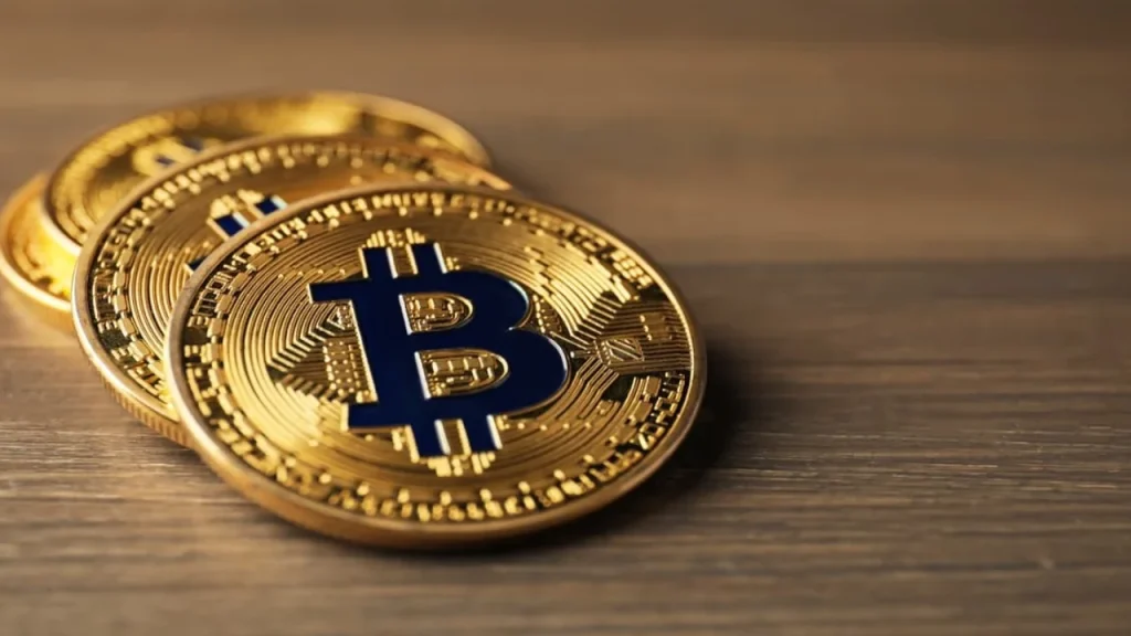Three gold Bitcoin coins with the blue B logo stacked and leaning against each other on a wooden surface.