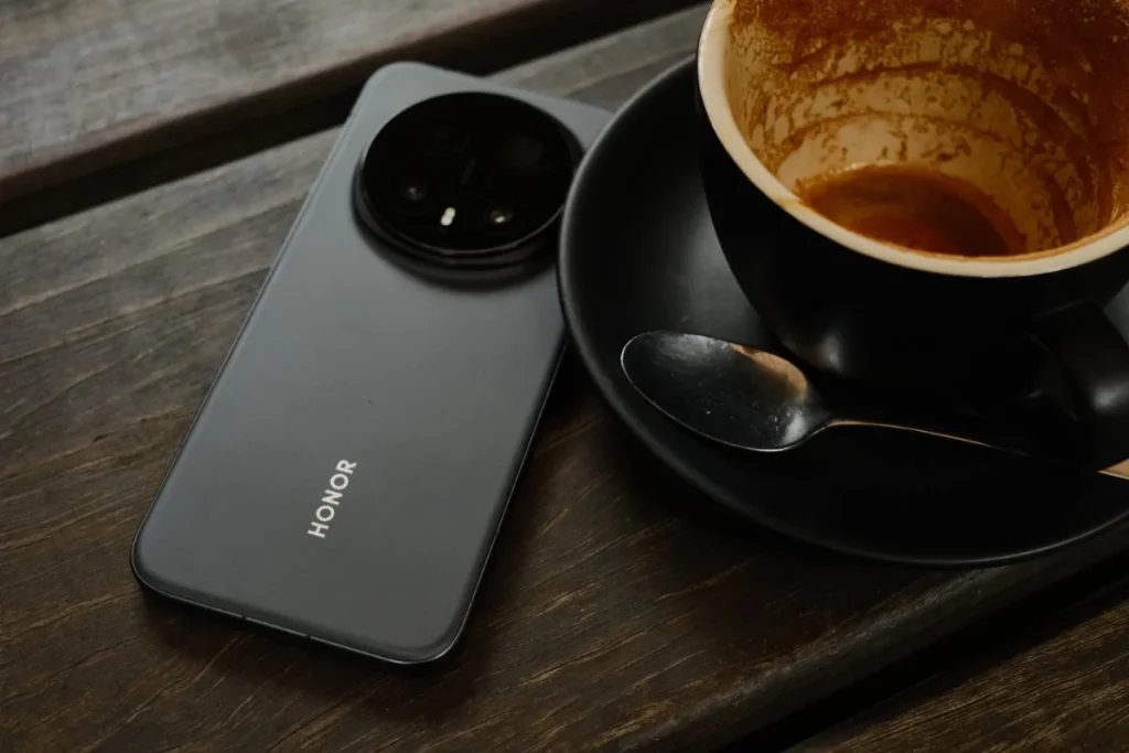 Honor Magic 8 Pro in black finish with circular camera island resting beside a coffee cup