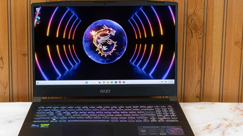 An open MSI Katana 15 HX laptop with a colorful RGB backlit keyboard and a dragon logo desktop wallpaper, positioned against a rustic wood-paneled wall.