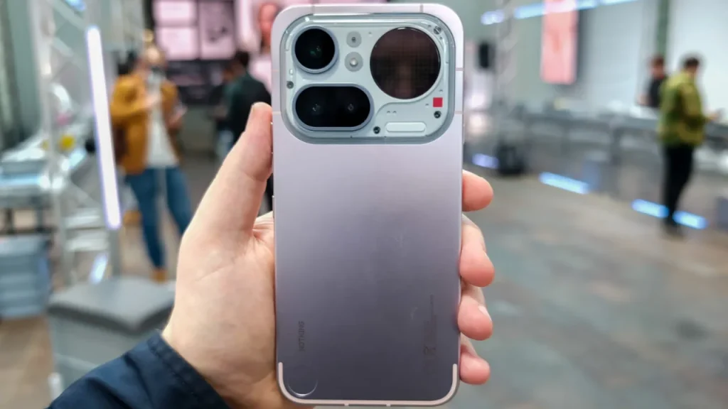 A hand holding a light purple Nothing Phone (4a), showcasing its unique transparent camera module design in an indoor setting.